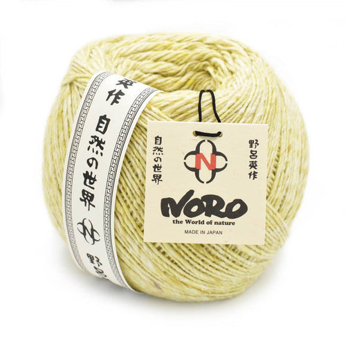 Close up of Noro Yarn in Moegi shade; Appears light yellow/green with white throughout; Shown from side with paper label wrapped around left outside edge in black and white with Japanese characters running up and down; Reads "NORO" "the World of nature" "MADE IN JAPAN" on tag tag attached with black tie on right side of yarn