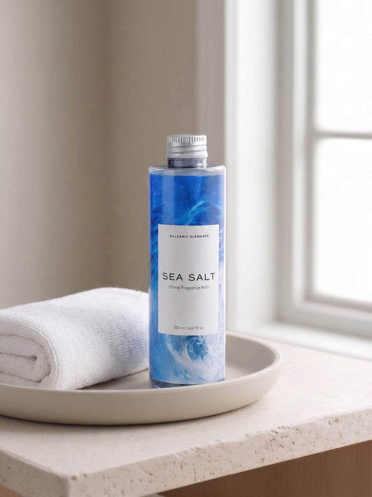 A bottle of Balearic Elements Sea Salt body wash stands on a beige tray next to a folded white towel, set on a windowsill with soft natural light.