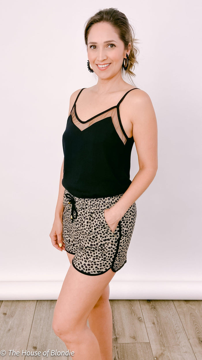 Woman wearing black mesh trim camisole and leopard print shorts posing indoors on wooden floor