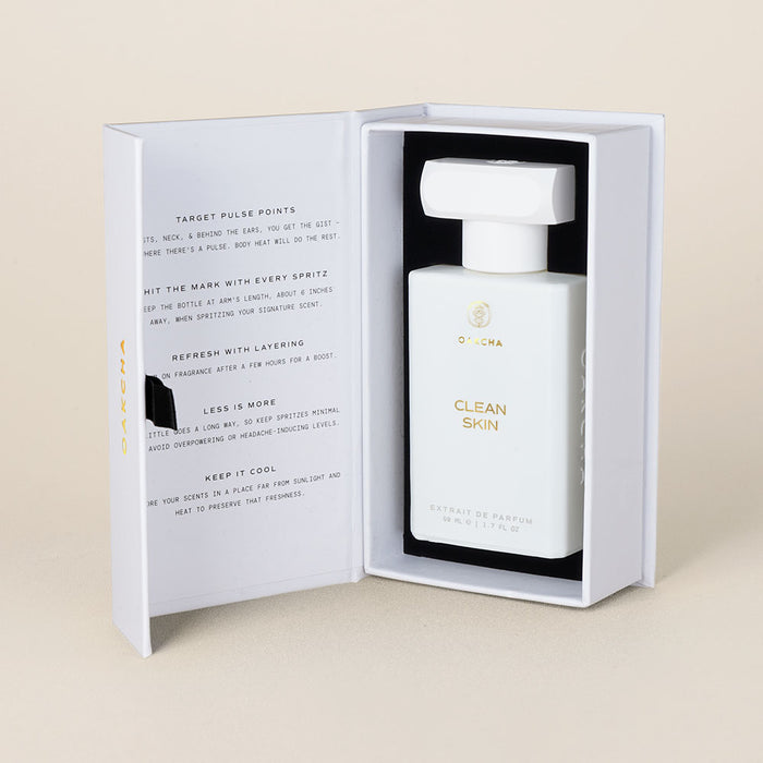 Front view of Clean Skin perfume bottle in open white presentation box showing gold logo on a beige background