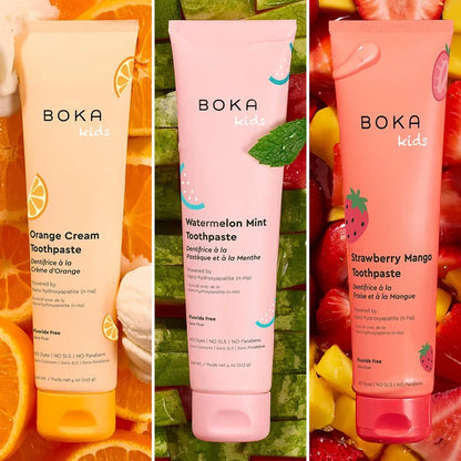 Three Boka Kids toothpaste tubes with fruit-themed designs on a colorful background.
