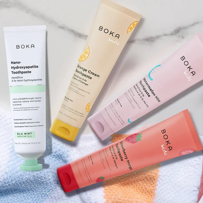 Four Boka Kids toothpaste tubes on a marble surface with a towel underneath.