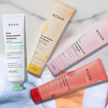Four Boka Kids toothpaste tubes on a marble surface with a towel underneath.
