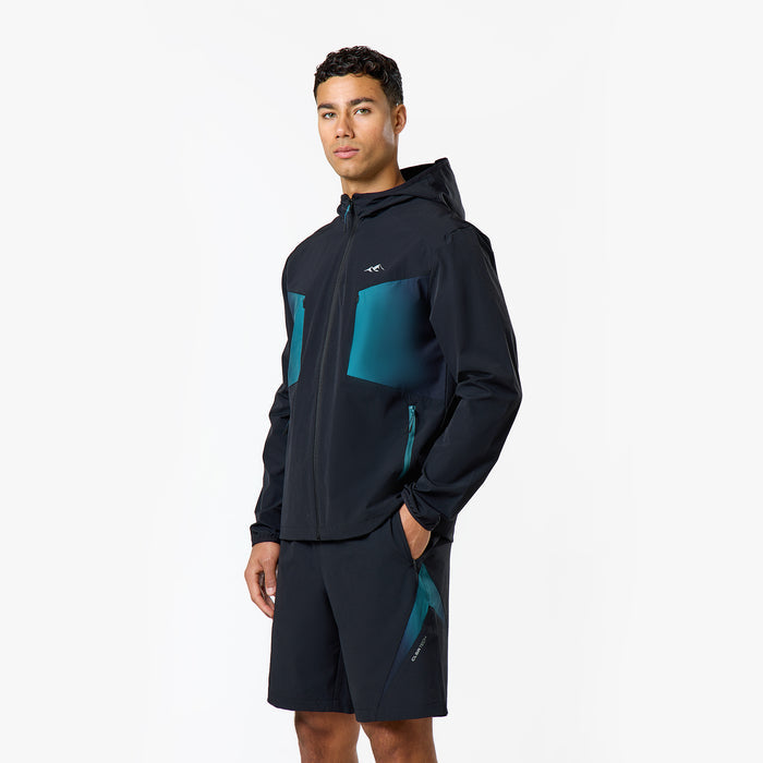 The model is wearing a teal detailed zip up windbreaker and black shorts with closure logo