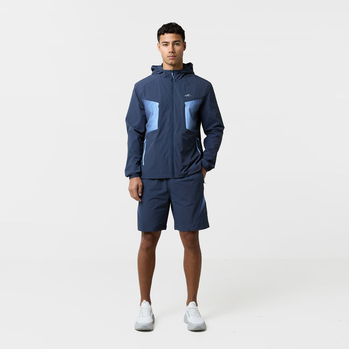 Model is wearing a tri-set with pair of navy shorts and a matching navy wind breaker featuring a logo and gradient shapes.