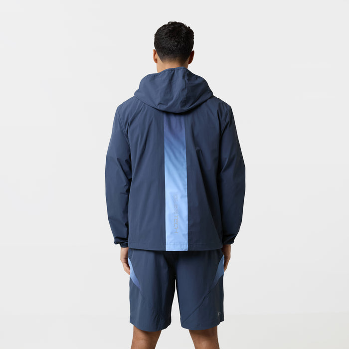 Model wearing tri-set is showing the back of navy windbreaker jacket with vertical gradient stripe and matching navy shorts