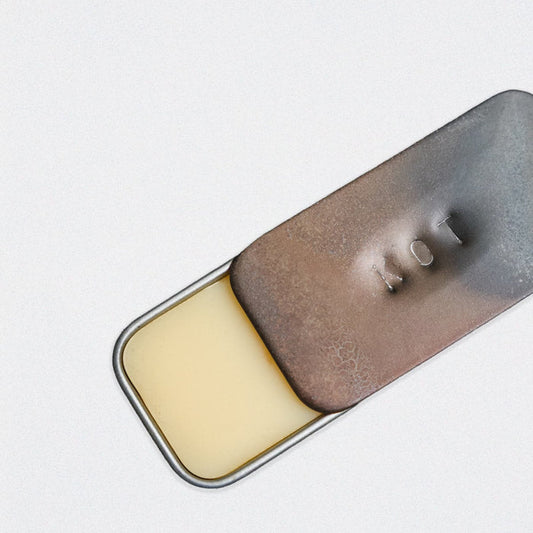 A close-up of a rectangular Fischersund KOT solid perfume metal tin with a hinged lid, partially open to reveal the pale yellow solid perfume itself. The lid has a textured, metallic finish with the name KOT embossed, set against a white background.