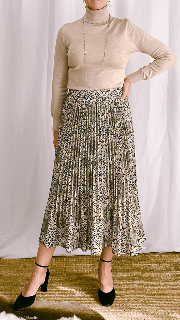 Woman wearing pleated midi skirt with intricate pattern and beige turtleneck sweater in boutique setting