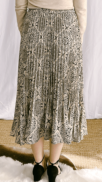 Back view of woman wearing Leonor pattern print midi pleated skirt with black and beige geometric design