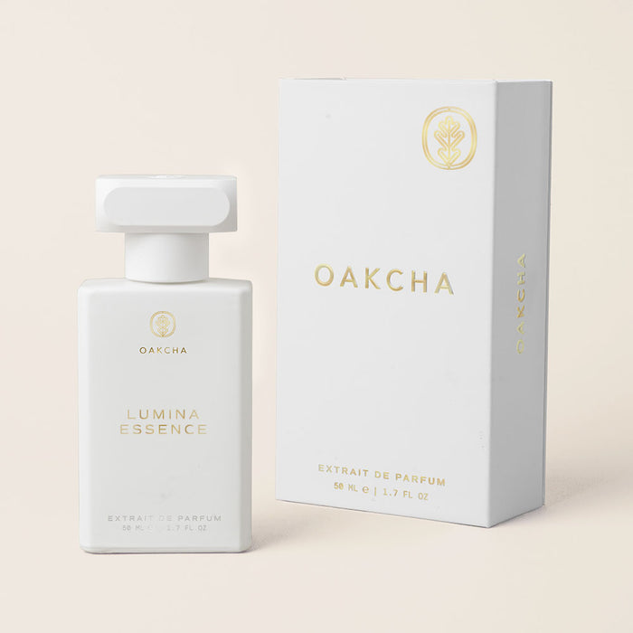 Front view of Lumina Essence Extrait de Parfum bottle and box showcasing white minimalist packaging with gold Oakcha logo on pale beige background