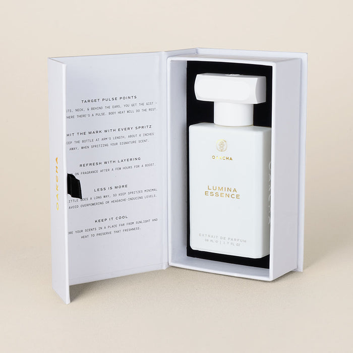 Front view of Lumina Essence extrait de parfum minimalist white bottle in open presentation box on beige background