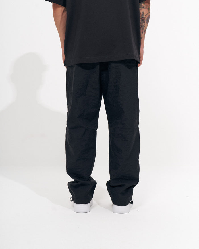 Martin Valen men's black baggy pant, side view showing hem and ankle drawcord detail with white-soled sneakers