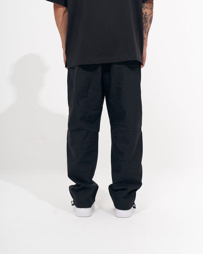 Martin Valen men's black baggy pant, side view showing hem and ankle drawcord detail with white-soled sneakers