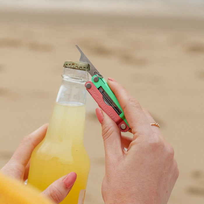 Person using the bottle opener on a Leatherman Micra® in Bayside color to open a bottle on the beach.
