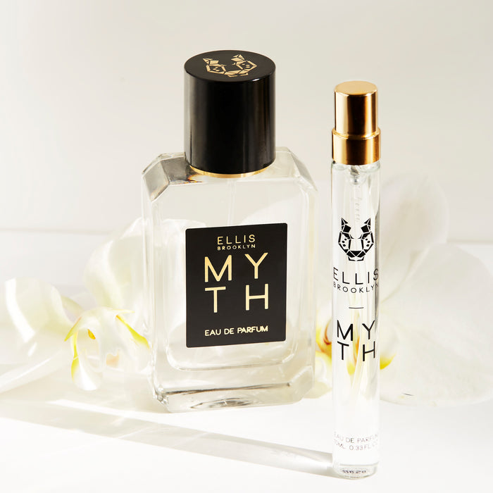Myth 50ml Eau De Parfum and Myth 10ml Eau De Parfum Travel Spray in front of white flowers on white background.