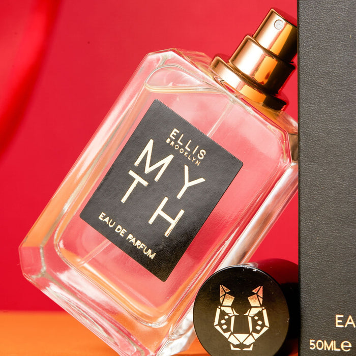 Myth 50ml Eau De Parfum with cap removed leaning on Myth 50ml Eau De Parfum box against red and orange background.