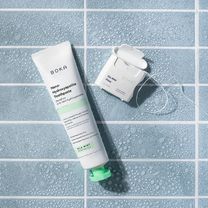 Boka toothpaste tube and dental floss on a tiled surface with water droplets.