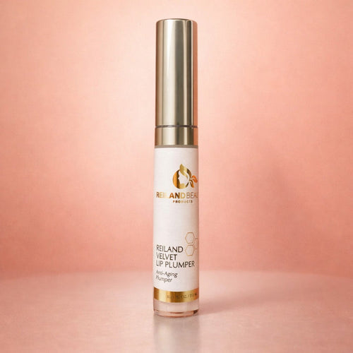 Reiland Velvet Lip Plumper displayed upright on a soft surface with a warm peach gradient background and gentle shadow.