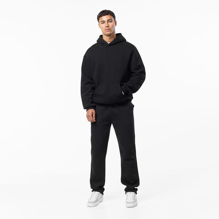 Model wearing relaxed fit tracksuit in black with one hand in the hoodie pocket