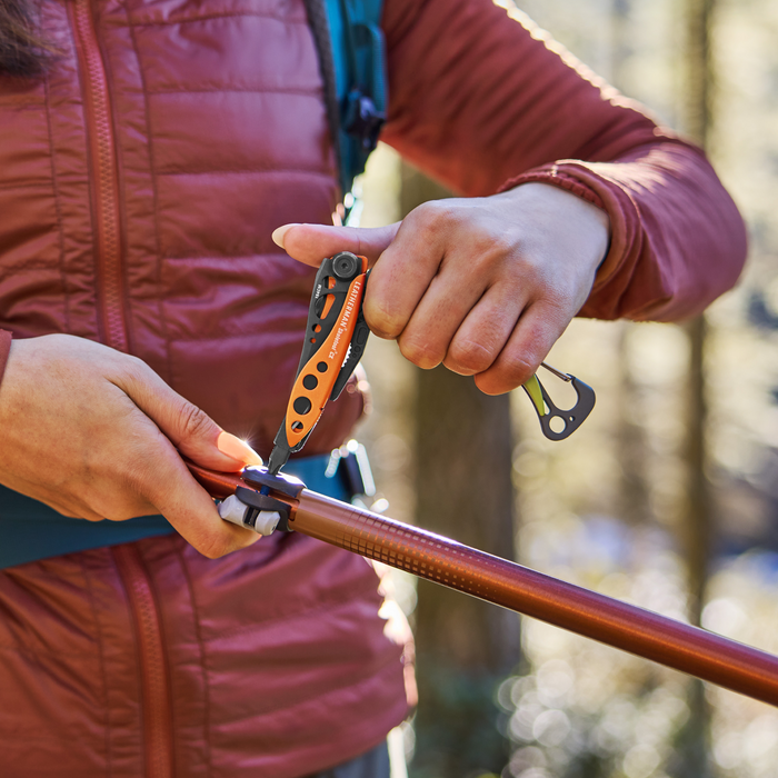 Person using a Leatherman Skeletool® CX in Aurora color to adjust a hiking pole outdoors.