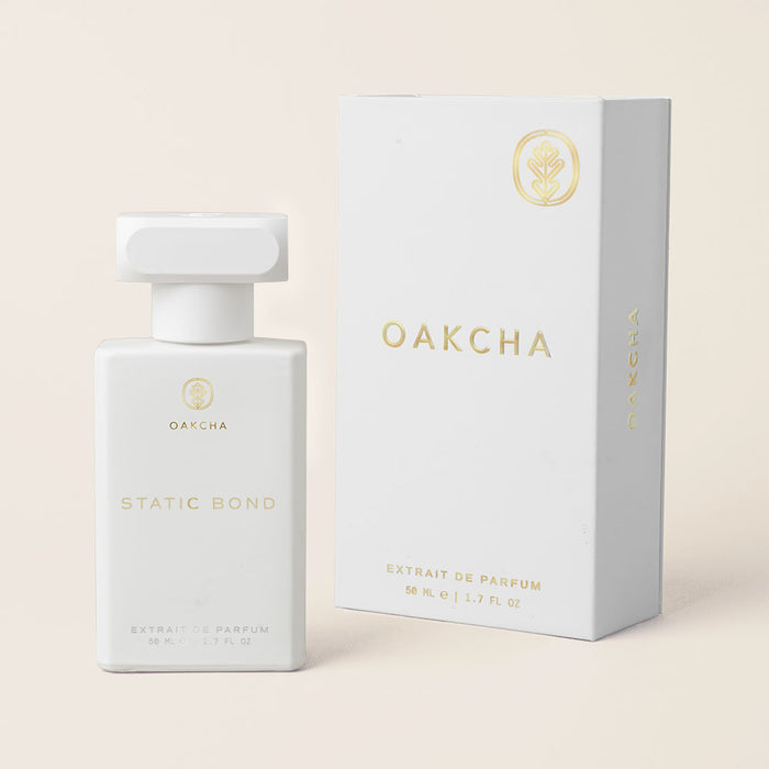 Front view of Static Bond perfume bottle and box showcasing white matte finish and gold lettering on a pale beige background