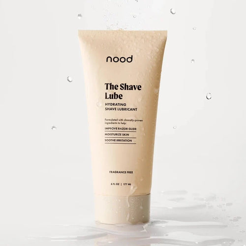Nood The Shave Lube hydrating shave lubricant tube with water droplets splashing around it on a light grey background