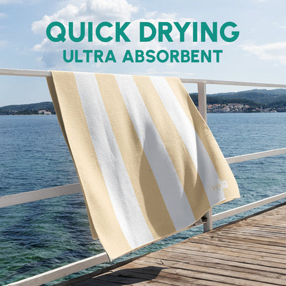 Waffle Microfiber Beach Towel - Natural Sand | SUN'Y hanging on a railing by the water, showcasing its quick drying and ultra absorbent fabric with beige and white stripes.