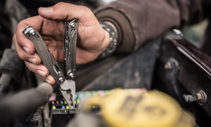 Hand using a stainless steel Leatherman Wingman® pliers to remove a fuse from a vehicle's electrical system.