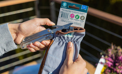 Hands using a stainless steel Leatherman Wingman® scissors to cut the zip tie from a garden glove package, showcasing its practicality outdoors.
